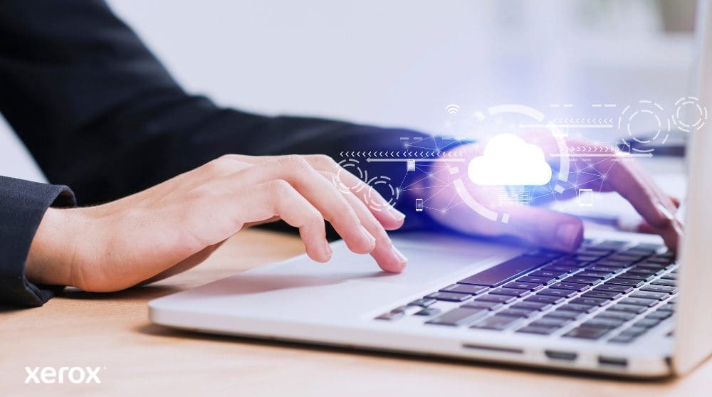 Sono raffigurate le mani di una persona che digita sulla tastiera di un computer portatile, con un'icona luminosa a forma di nuvola e connessioni di rete sovrapposte all'immagine, a simboleggiare la connettività cloud e i flussi di lavoro digitali.