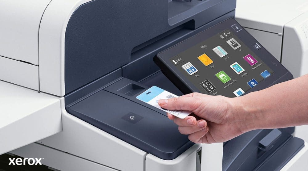 Una mano tiene una tessera di sicurezza e la scansiona vicino al lettore di una moderna stampante multifunzione Xerox, dotata di un ampio display touchscreen che mostra varie icone di applicazioni.